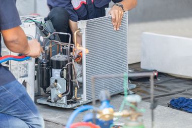 Technicians working on a large industrial machine outdoors beside a gray wall