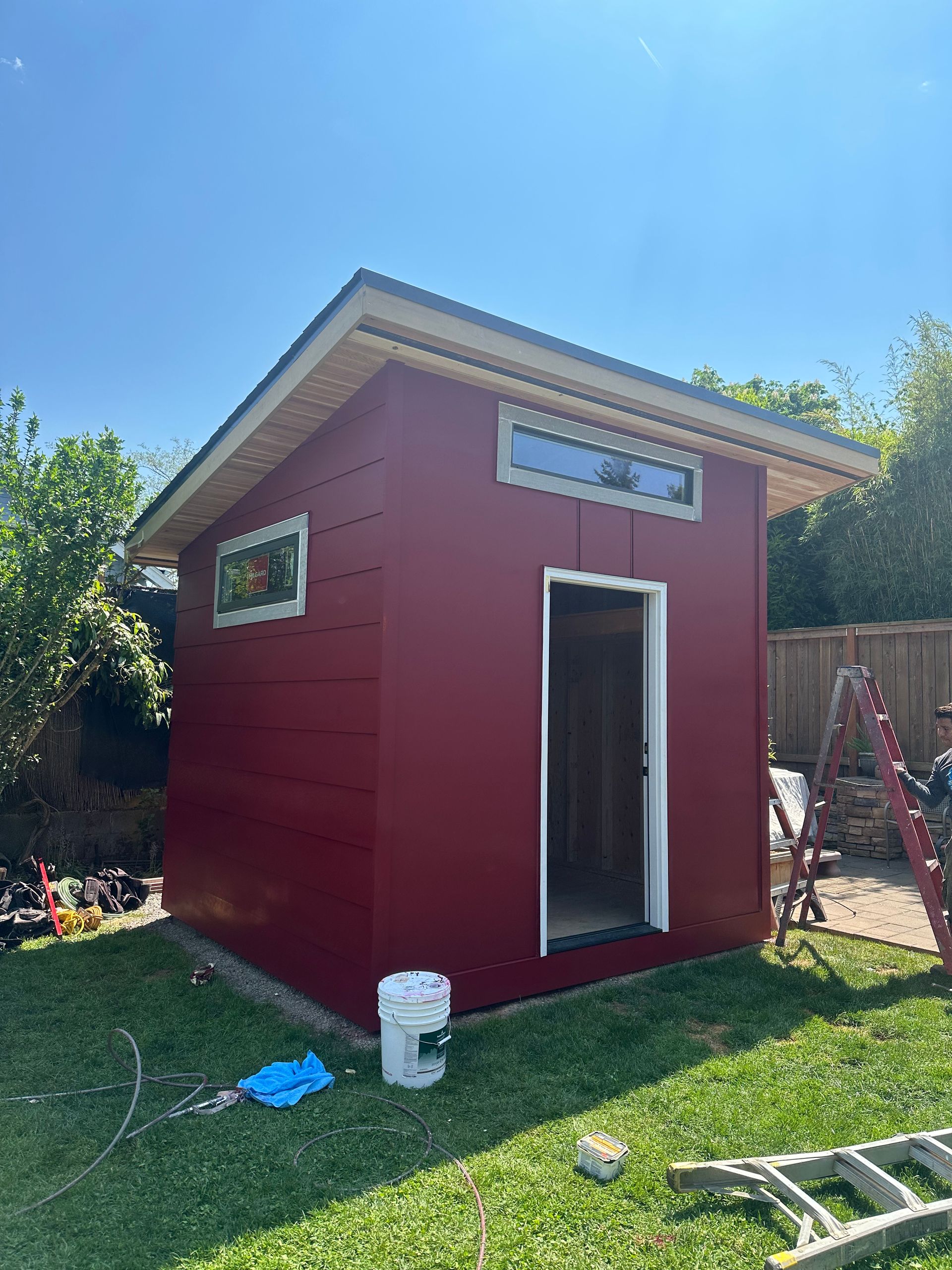 A red shed is being painted in a backyard.