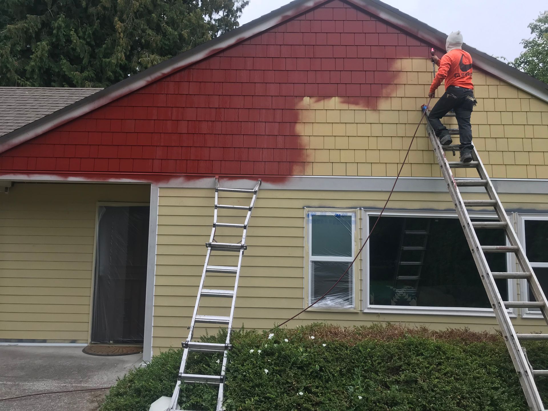 A man on a ladder is painting the side of a house