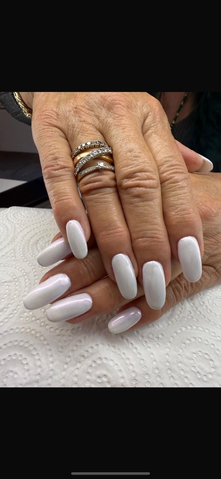 Un primo piano delle mani di una donna con unghie bianche e anelli.