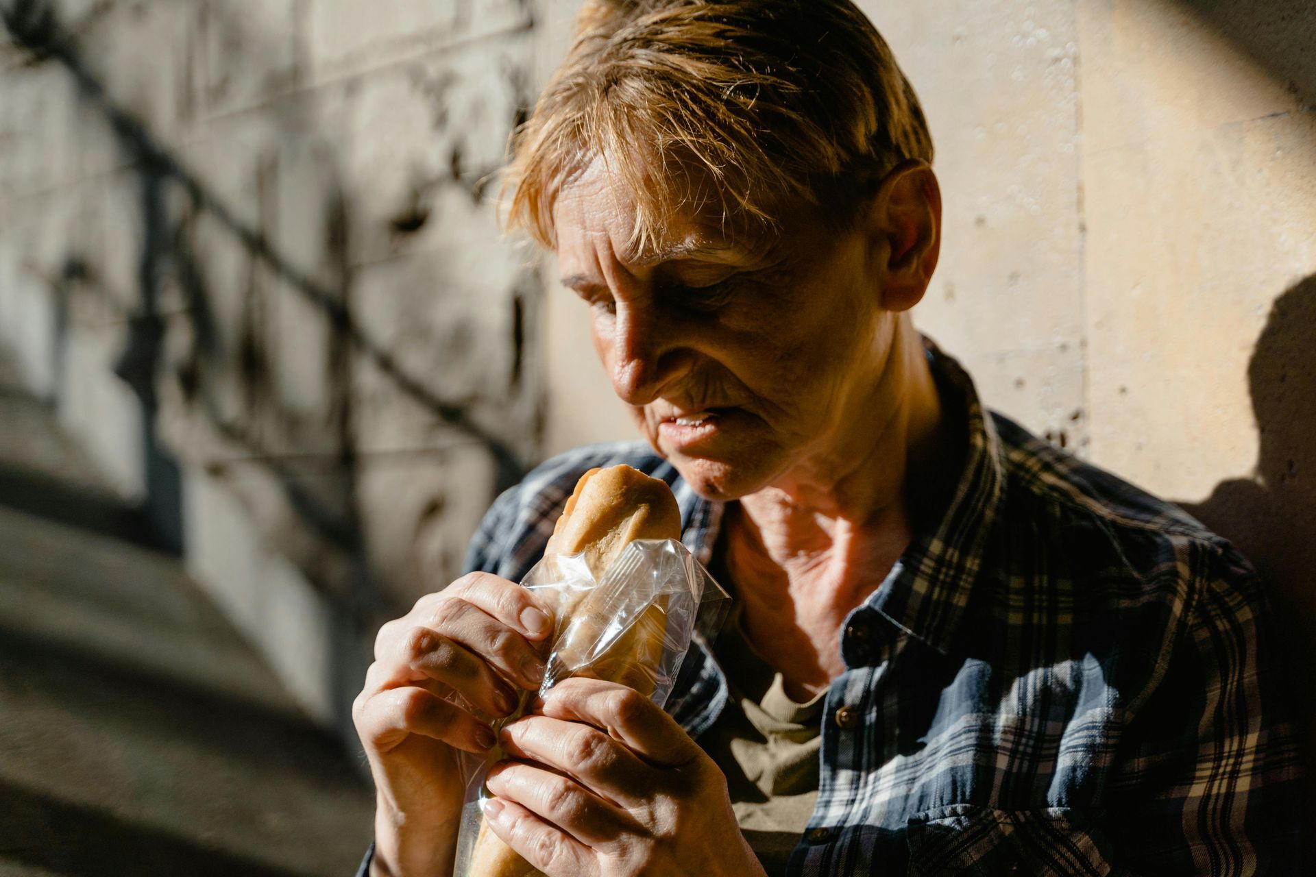 Person holding a baguette, against a light-toned wall. They appear to be struggling to open the packaging.