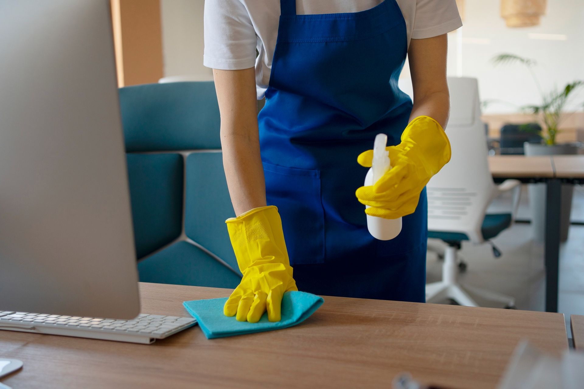 A woman is cleaning a desk with a cloth and spray bottle.