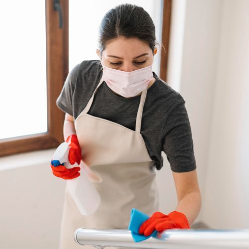 A woman wearing a mask and apron is cleaning a railing.