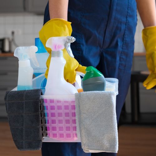A person wearing yellow gloves is carrying a basket of cleaning supplies.