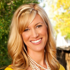 A woman wearing a yellow shirt and a pearl necklace smiles for the camera