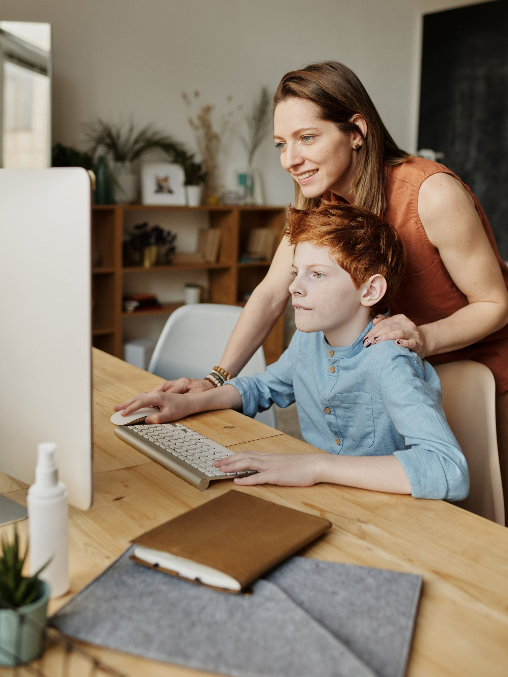 A woman is standing next to a boy using a computer.