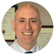 A bald man in a white coat and tie smiles for the camera