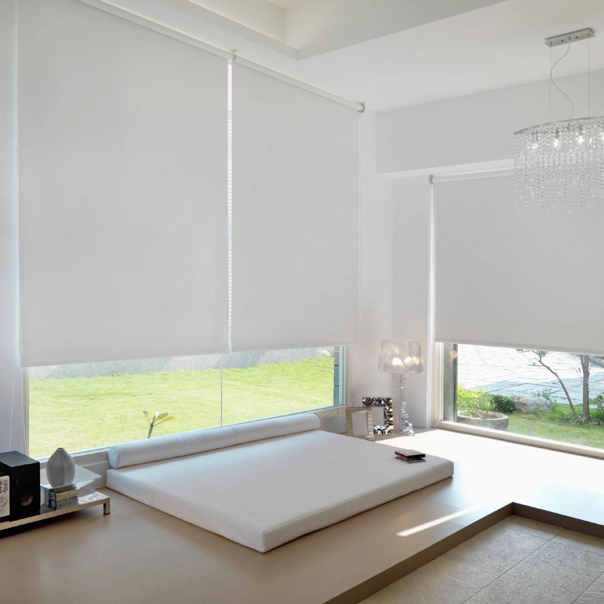 Habitación con persianas enrollables blancas, una cama tipo plataforma y una lámpara de araña.