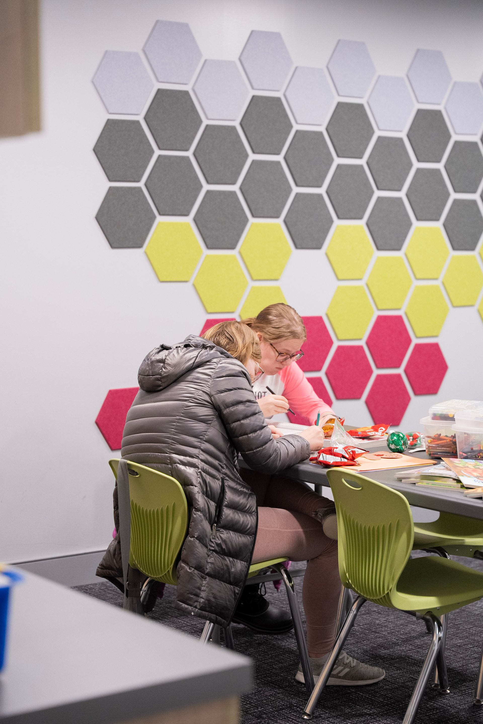 A woman is sitting at a table in front of a wall with hexagons on it.