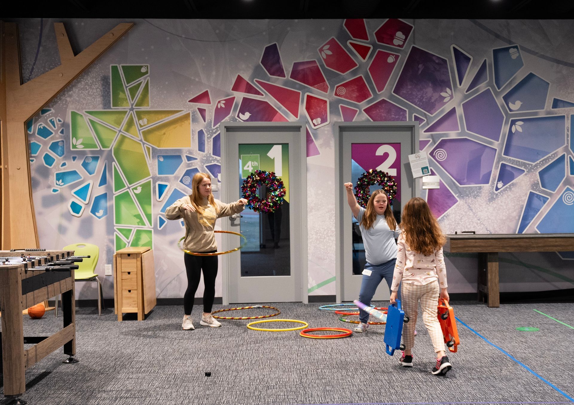 Two girls are playing in a room with a painted stained glass wall.