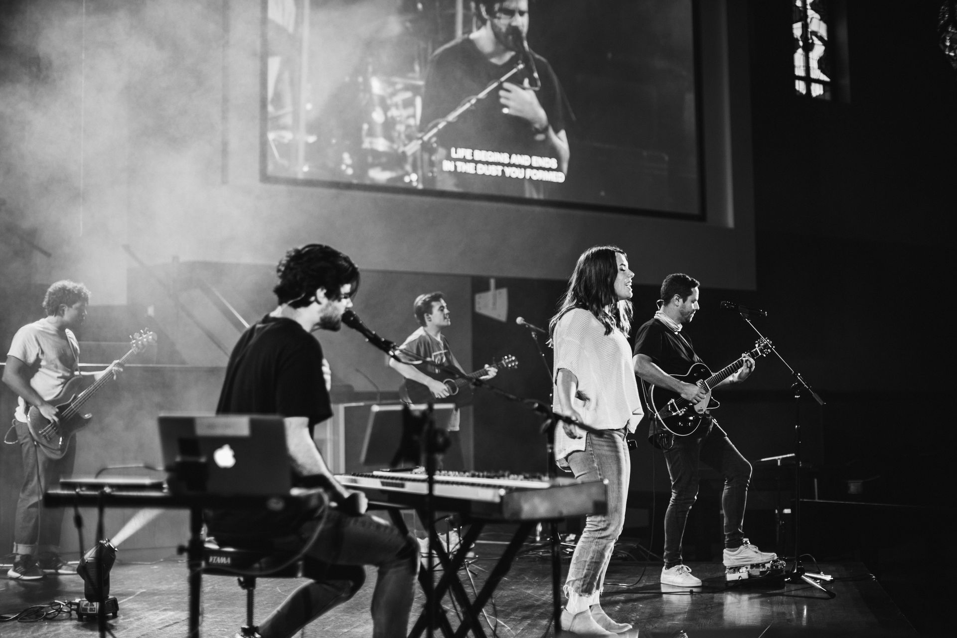 A black and white photo of a group of people playing instruments on a stage.