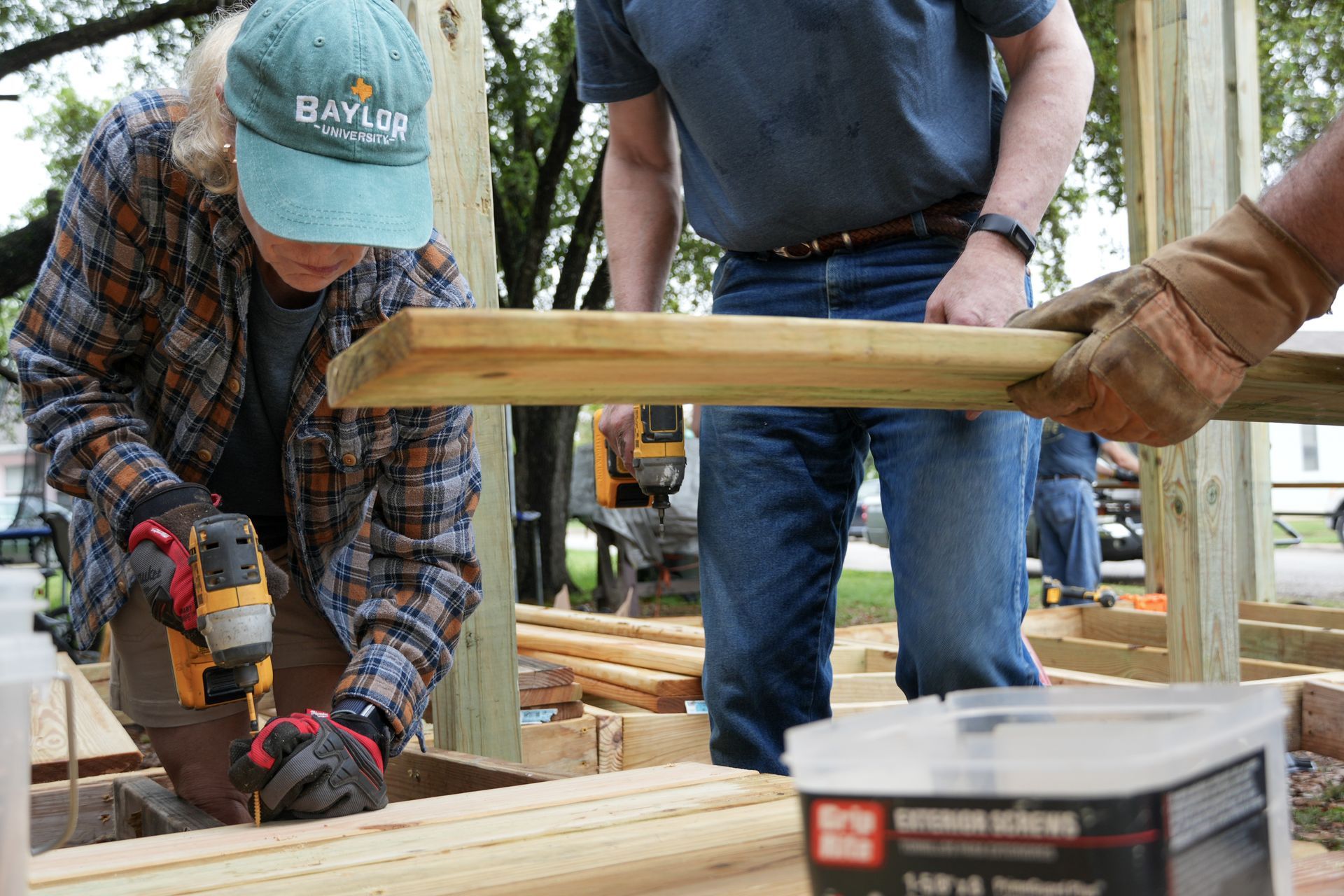 A man is lifting a piece of wood in a yard.