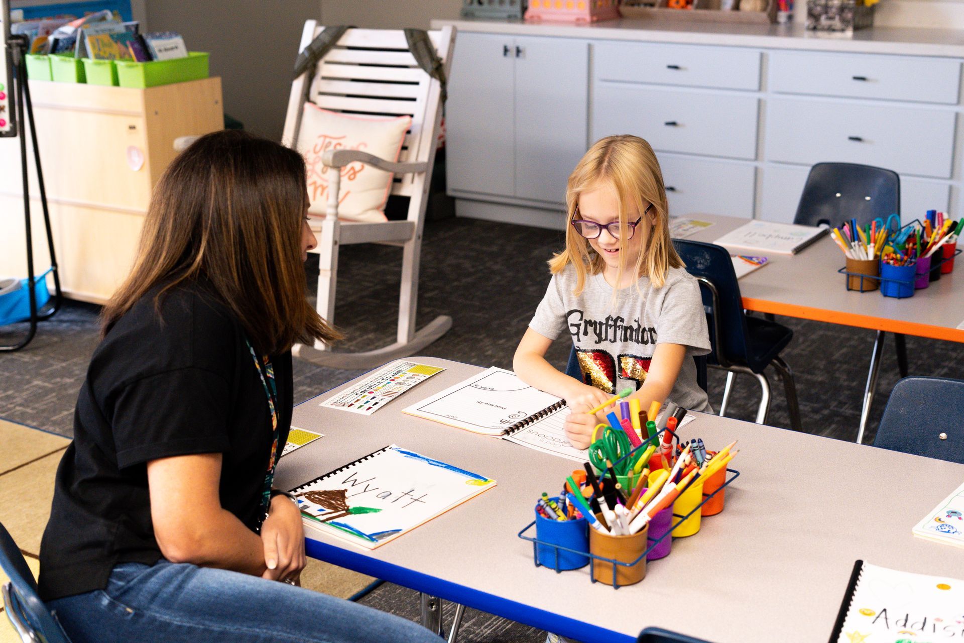 A woman is sitting at a table with a girl in a classroom.