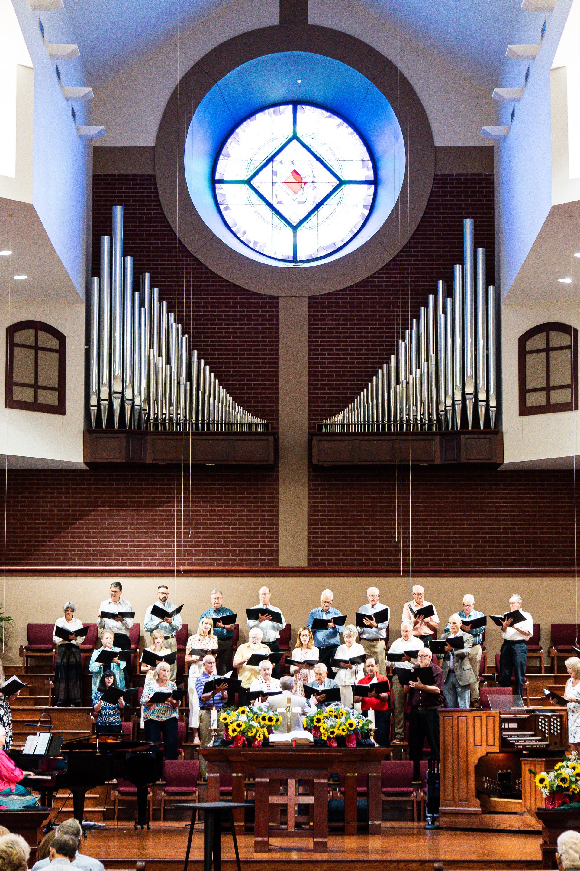 A choir is singing in a church with a stained glass window