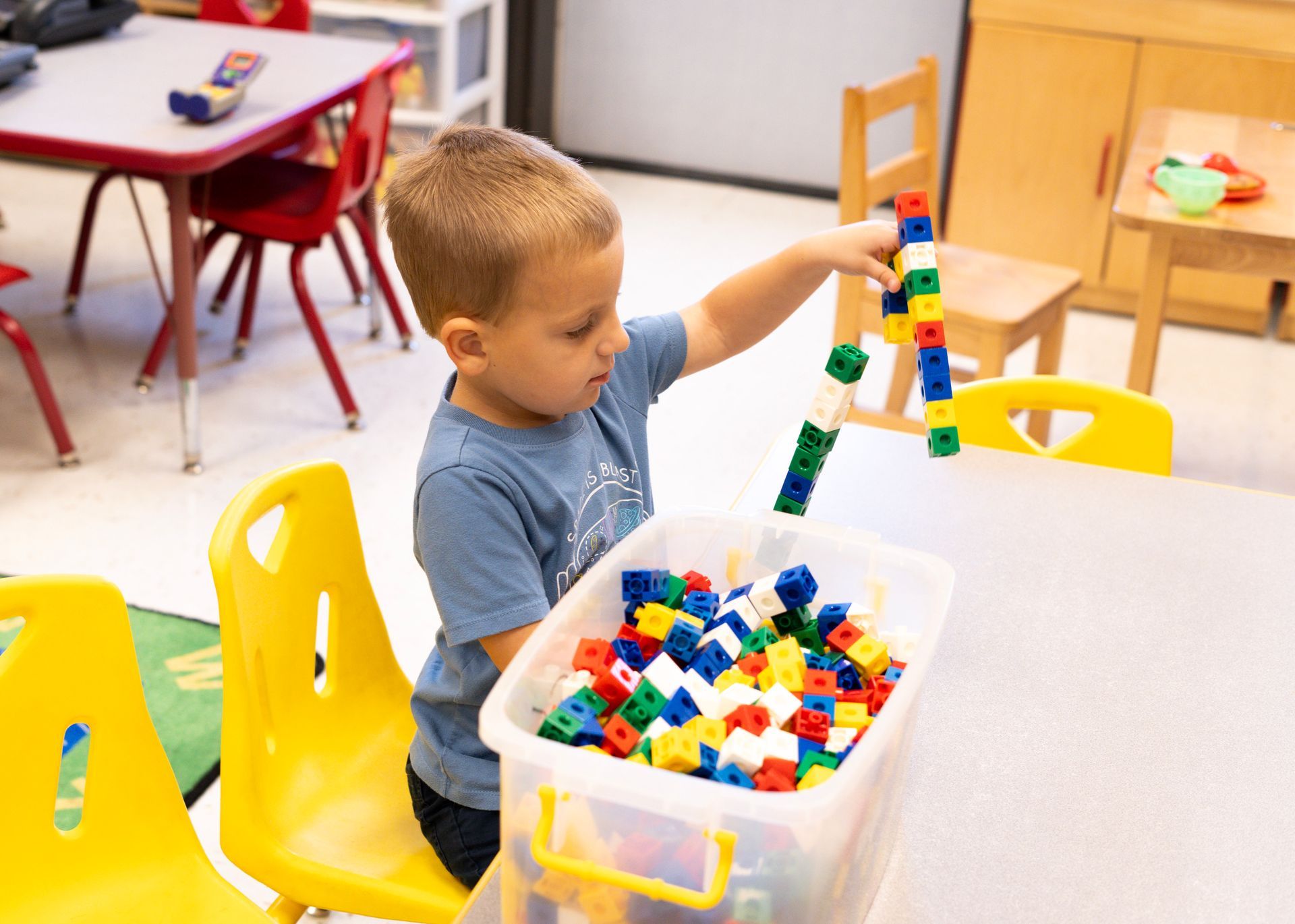 A young boy is playing with lego blocks in a classroom.
