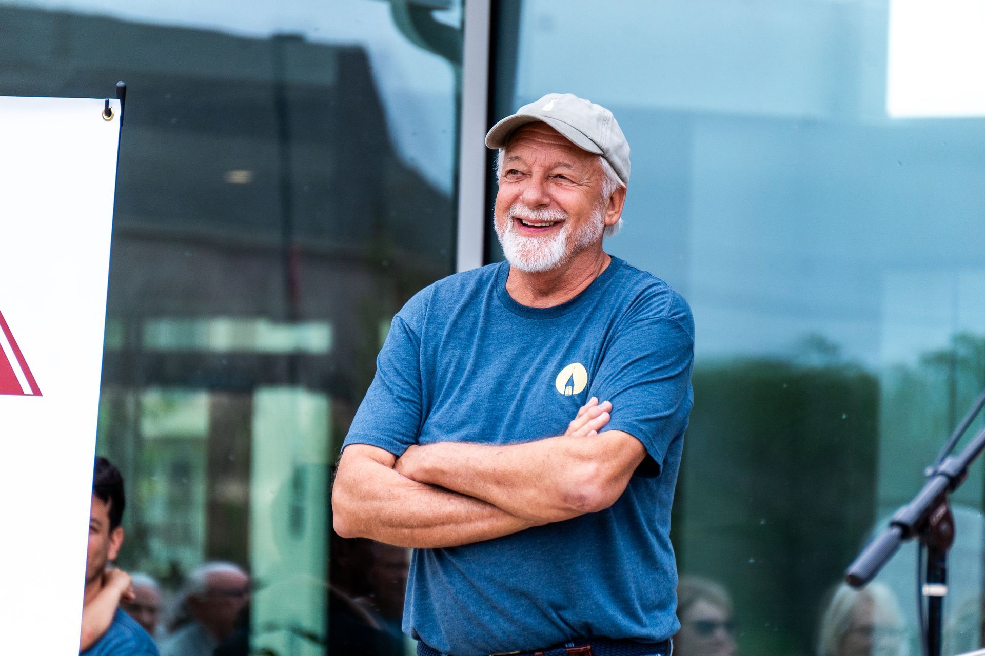 A man with a beard is standing with his arms crossed in front of a microphone.