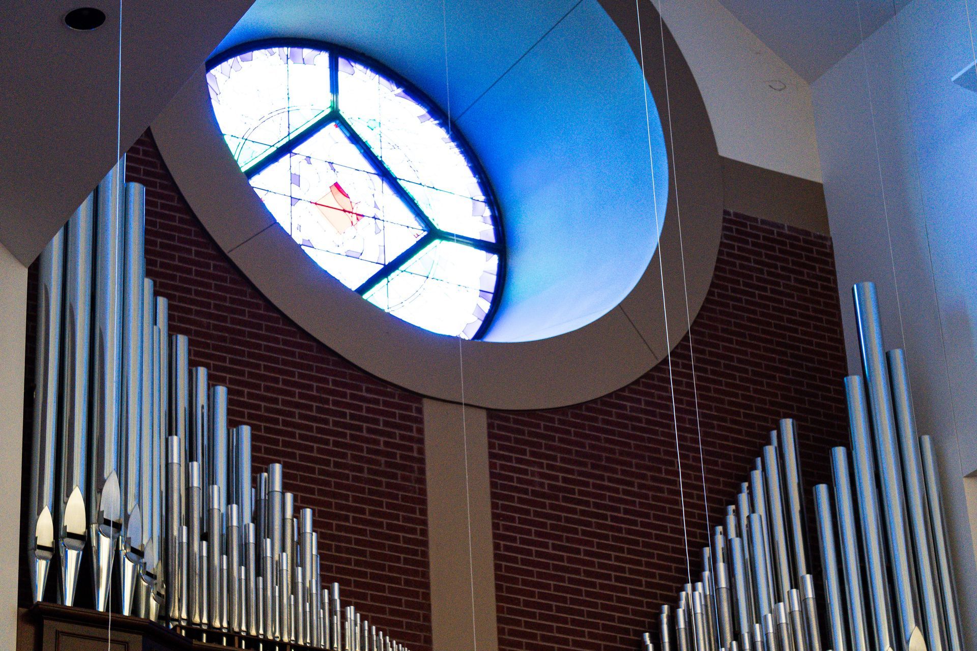 Organ pipes against a brick wall with a large, arched stained-glass window. Christ Church in College Station TX
