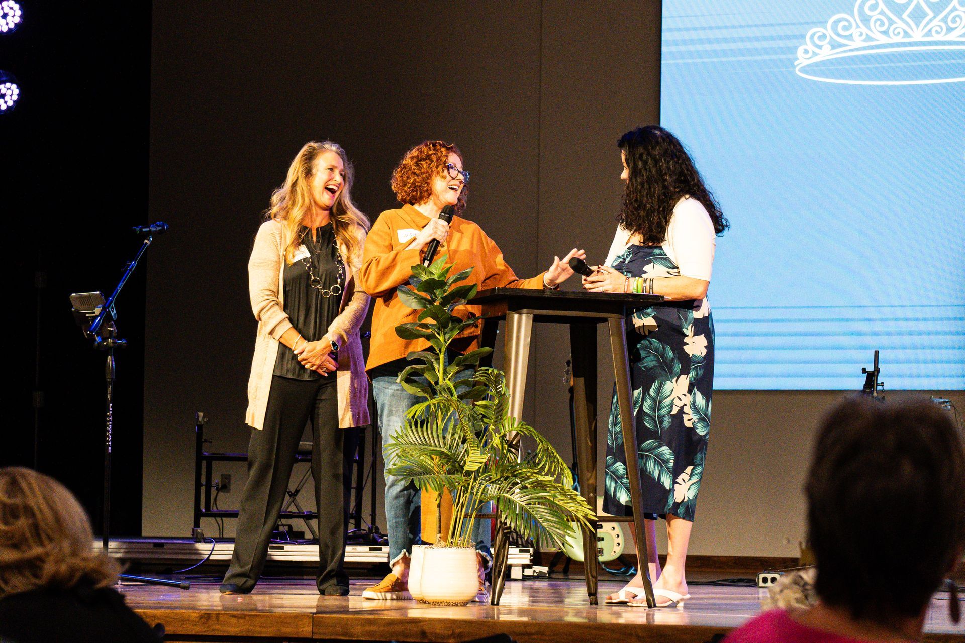 Three women are standing on a stage talking to each other.