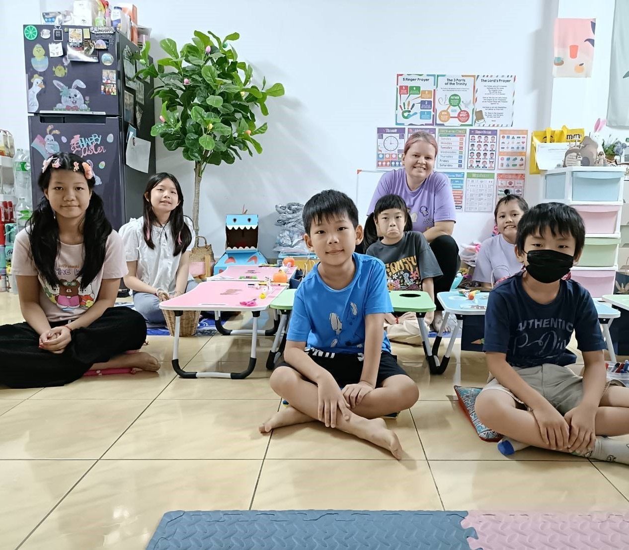 Children and a teacher sitting in a classroom, some on the floor, some at small tables - Christ Church cross cultural workers