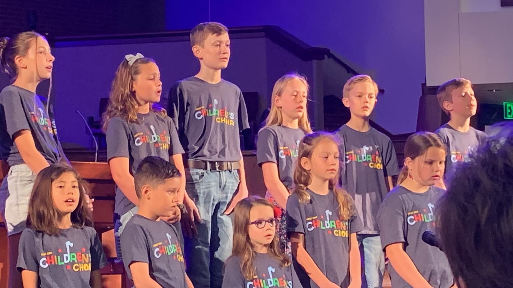 A group of children are singing in a choir in a church.