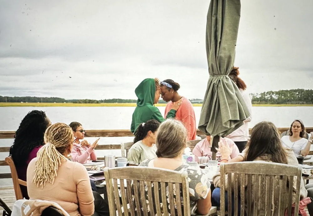 A group of people are sitting at a table in front of a body of water.