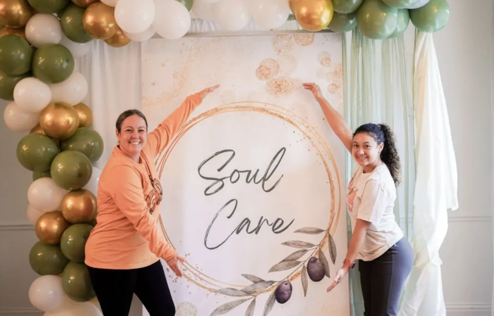 Two women are standing in front of a sign that says soul care.