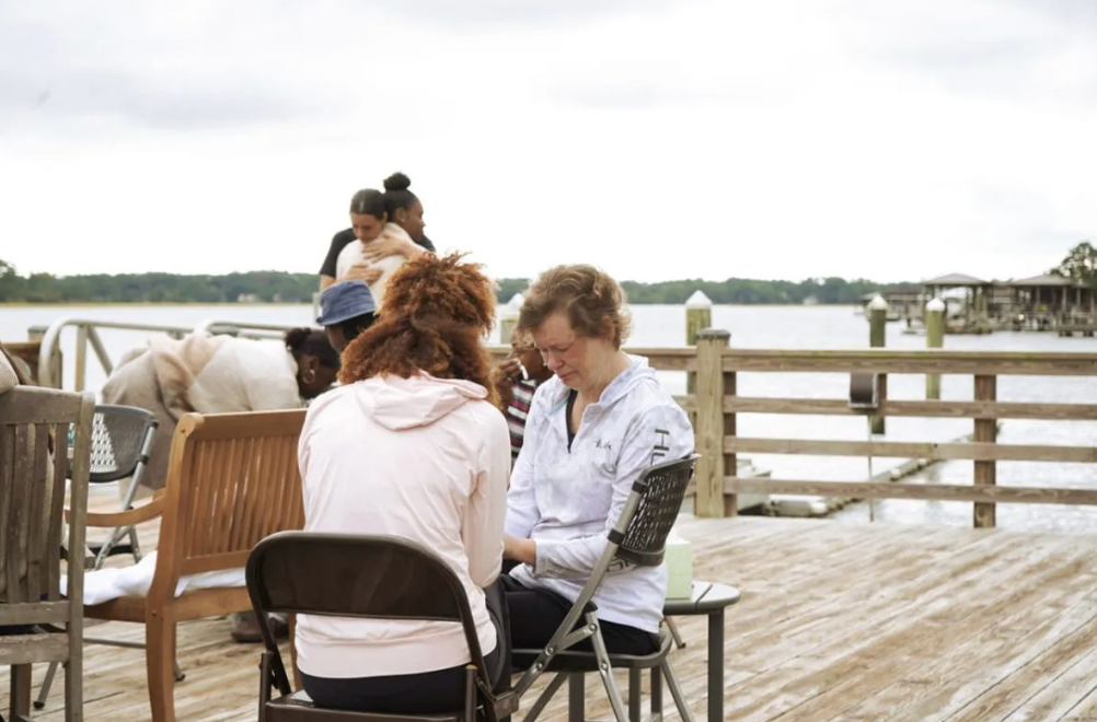 A group of people are sitting on a wooden deck overlooking a body of water.
