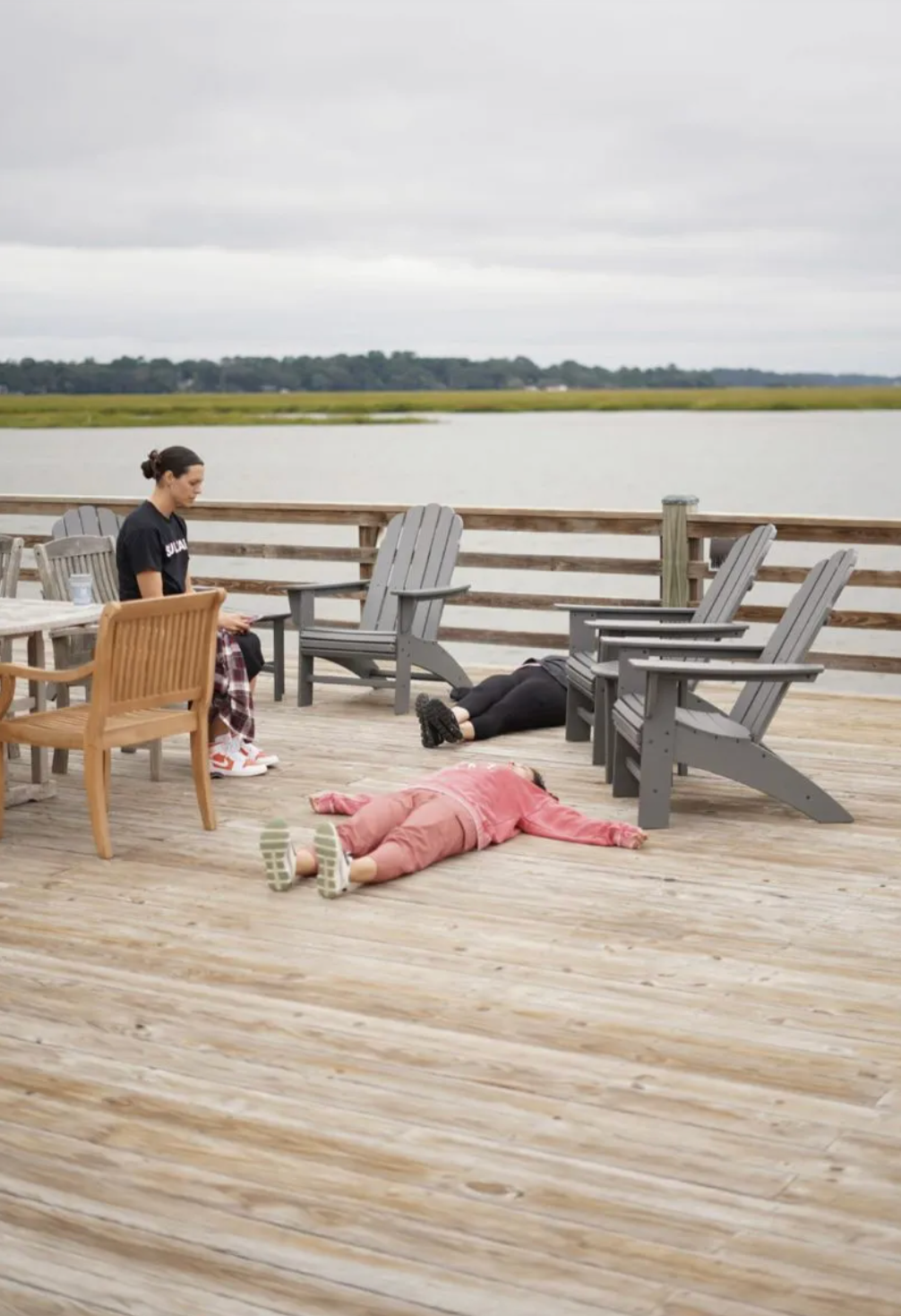 A little girl is laying on the ground on a wooden deck.