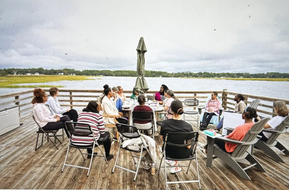 A group of people are sitting on a wooden deck overlooking a body of water.
