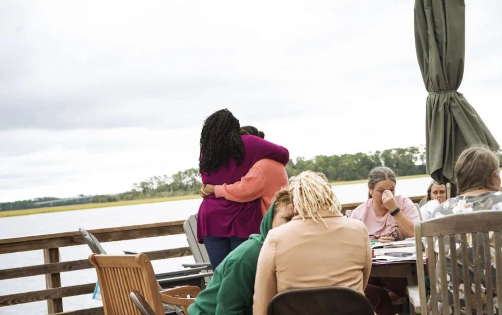 A group of people are sitting at a table on a dock hugging each other.