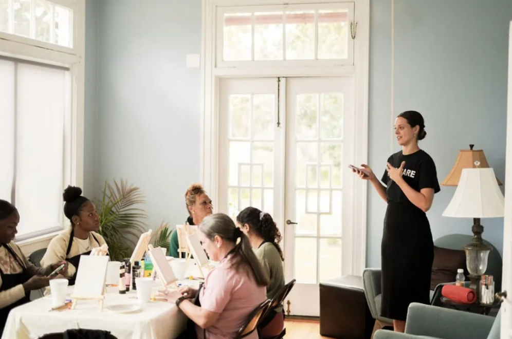 A woman is standing in front of a group of people sitting at tables.