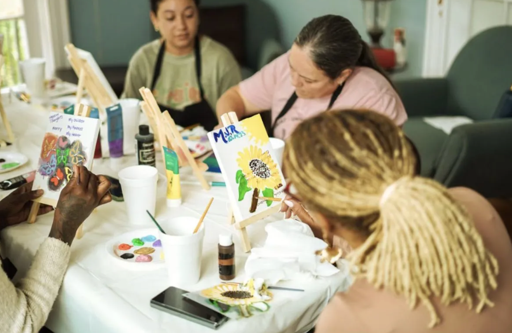 A group of people are sitting around a table painting.