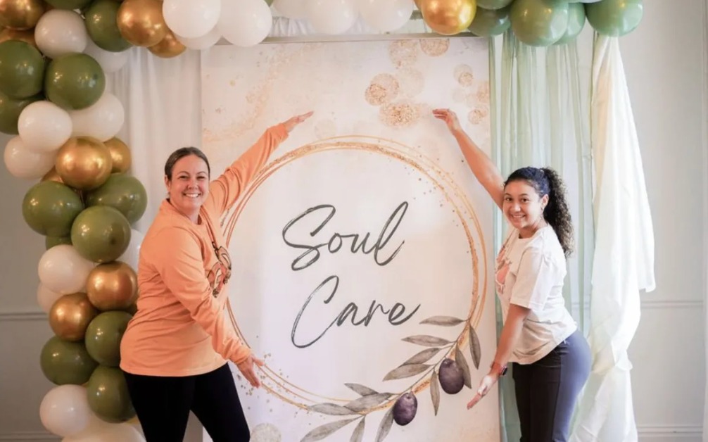 Two women are standing in front of a sign that says soul care.