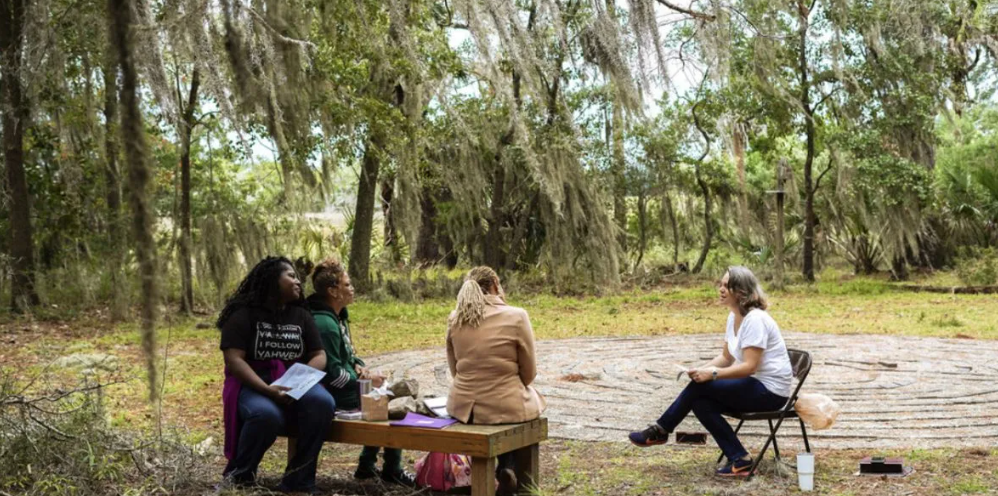A group of women are sitting around a table in the woods.