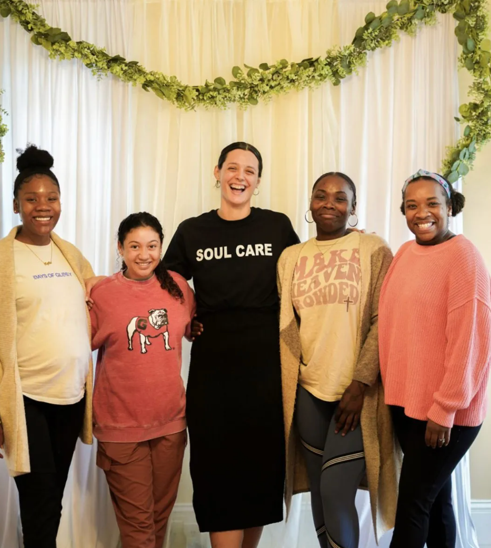 A group of women posing for a picture with one wearing a soul care shirt