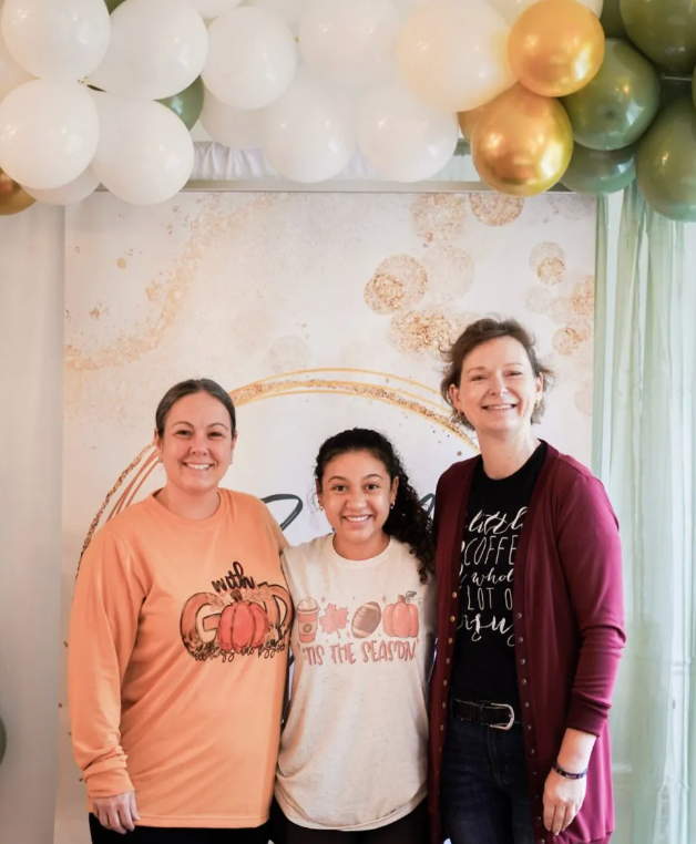Three women are posing for a picture in front of balloons