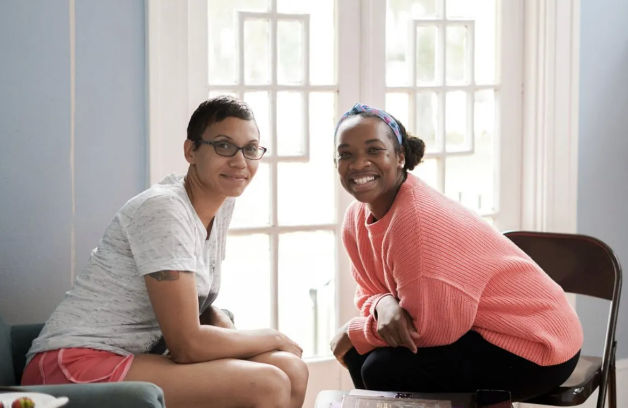 Two women are sitting next to each other in front of a window.