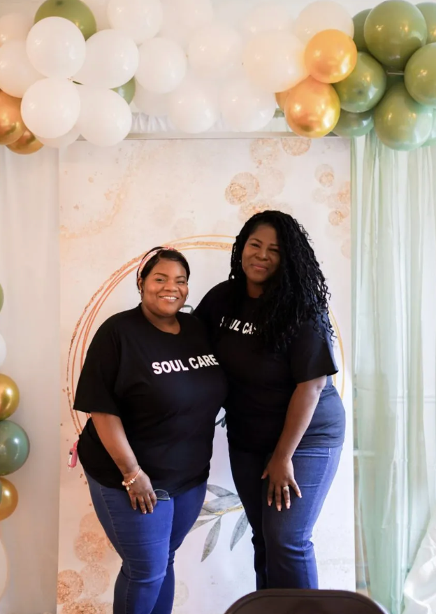 Two women are posing for a picture in front of balloons.