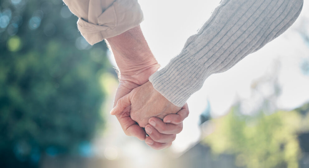 An elderly couple is holding hands in a park.