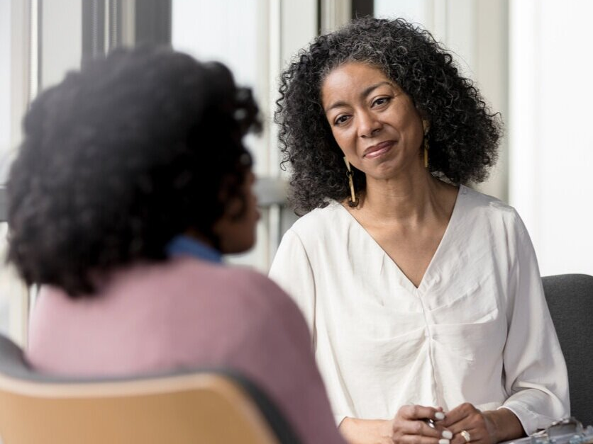 A woman is sitting in a chair talking to another woman.