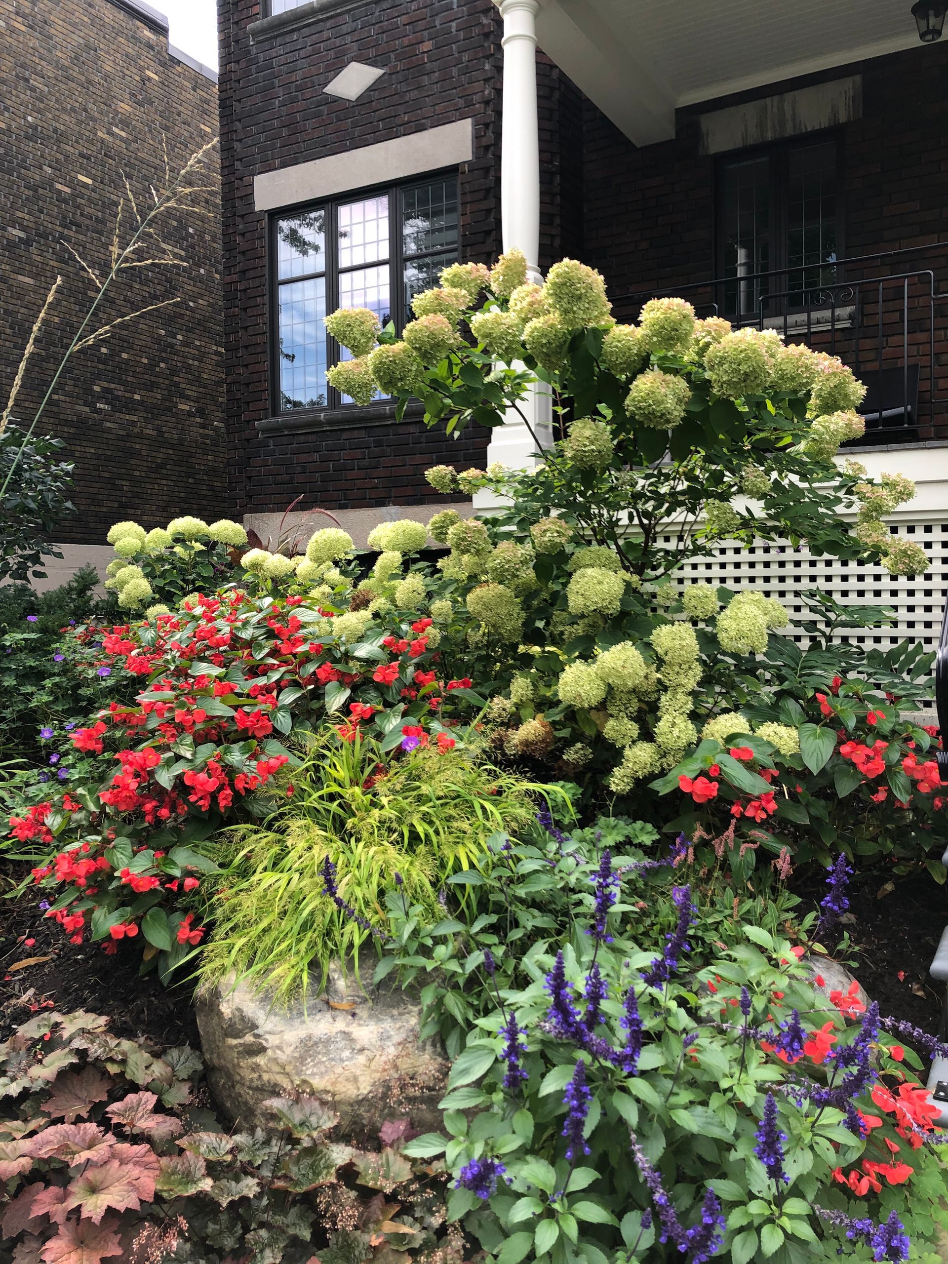 Un jardin avec beaucoup de fleurs et de plantes devant une maison en briques.