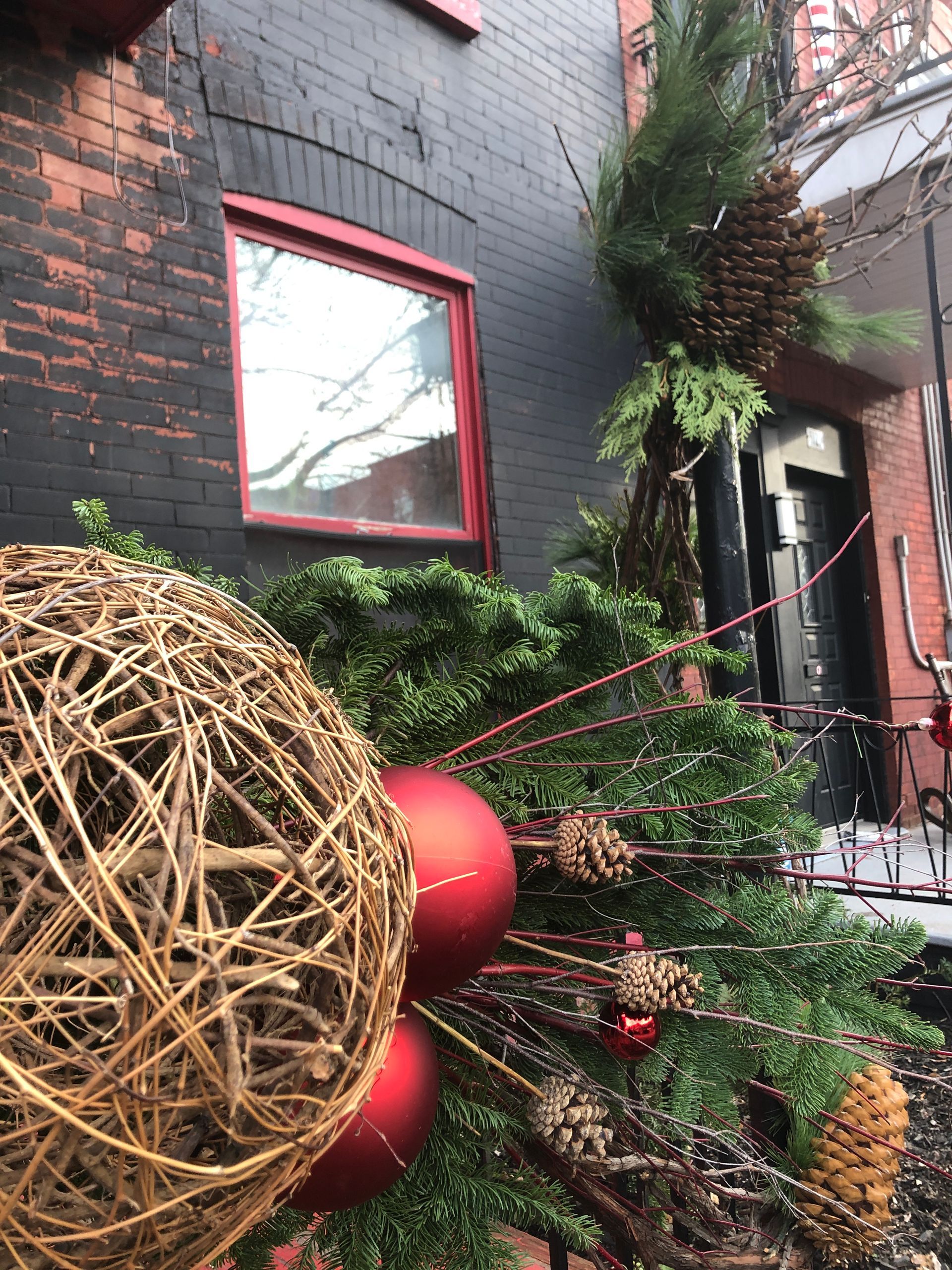A christmas tree with red balls and pine cones in front of a brick building.