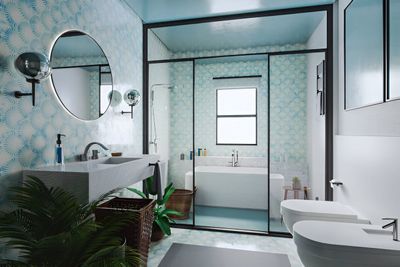 A modern bathroom with light blue walls and a large round mirror over a concrete vanity. A shower and bathtub are visible through a glass door.