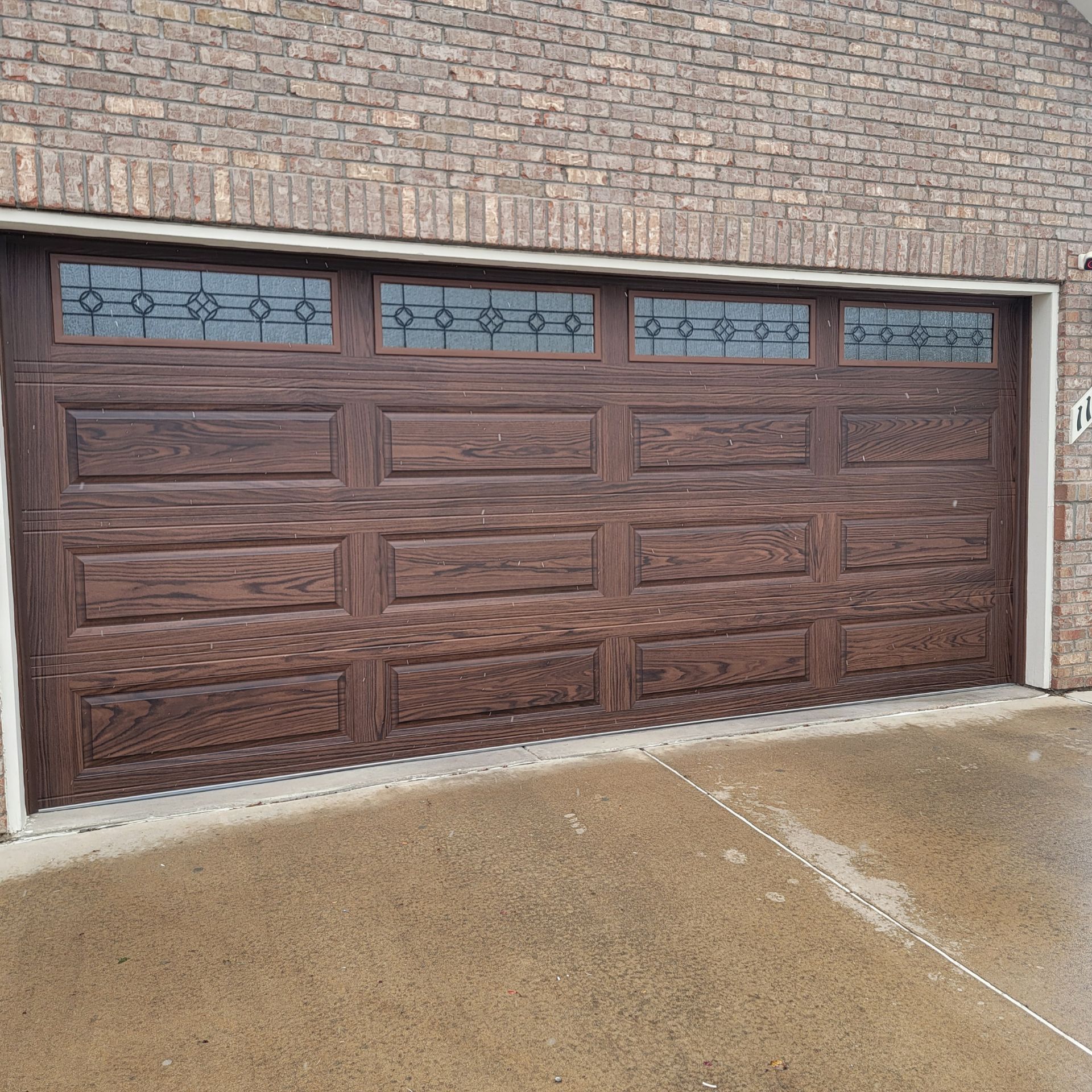 Brown garage door with decorative glass panels above, set in a brick building.