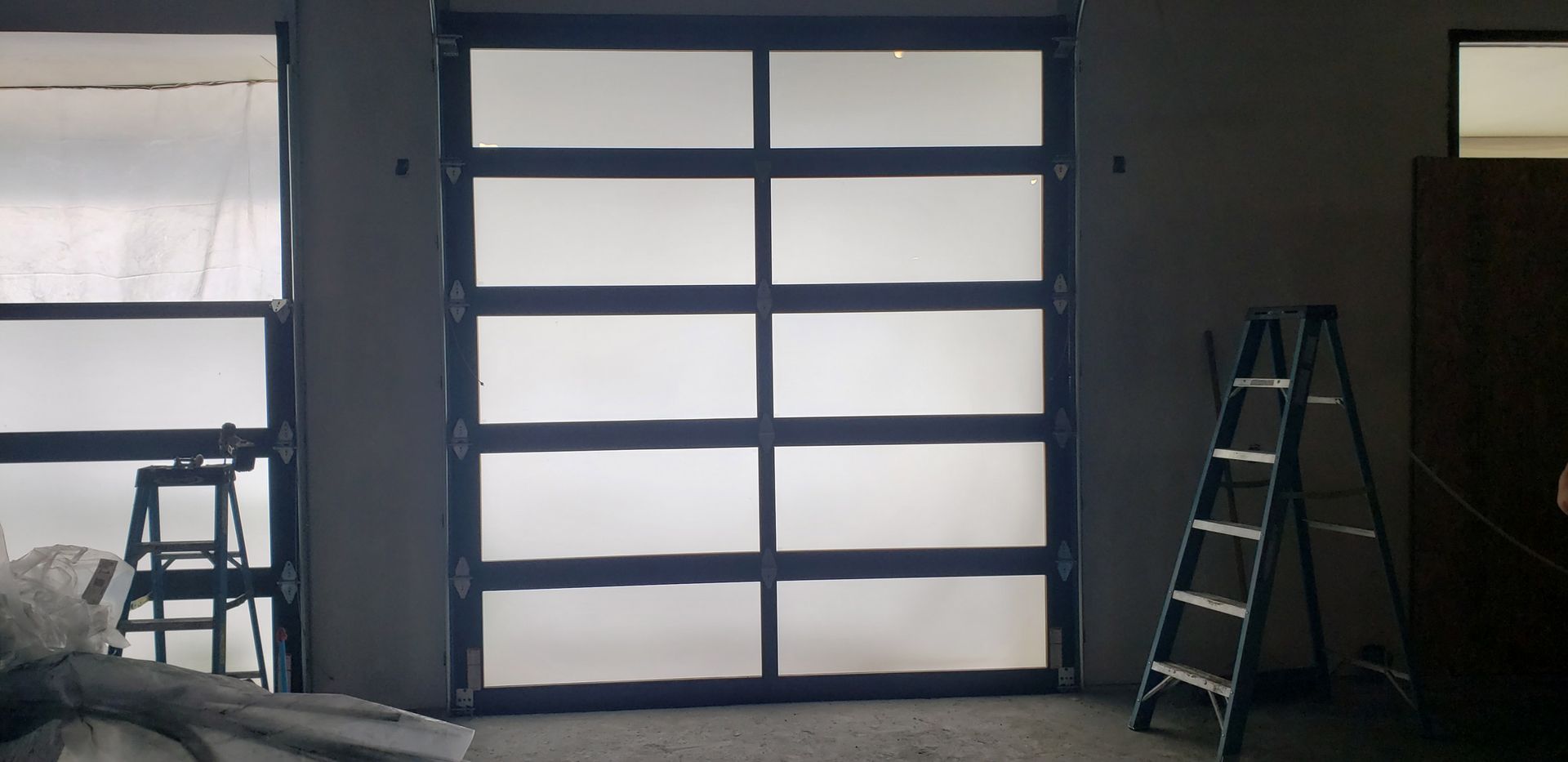 A large, modern garage door with frosted glass panels. A ladder is leaning against the wall.