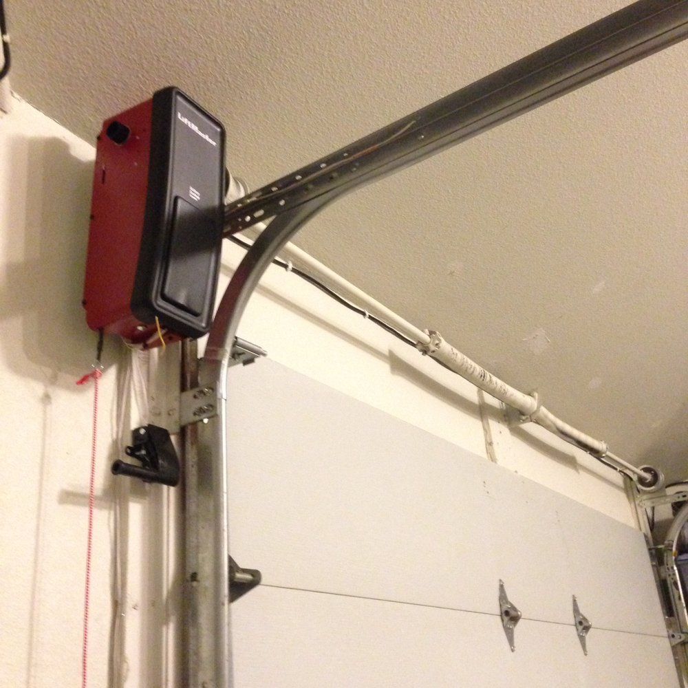Red garage door opener attached to the ceiling with metal track, opening the white garage door.