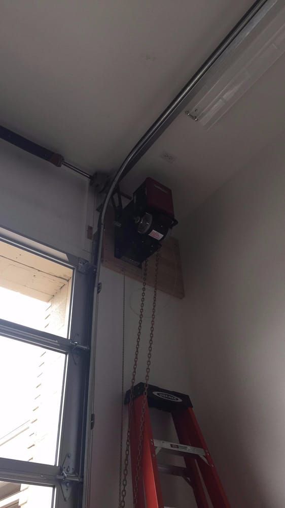 Garage door opener mounted on a wooden board; a chain hangs down, and a red ladder stands below.