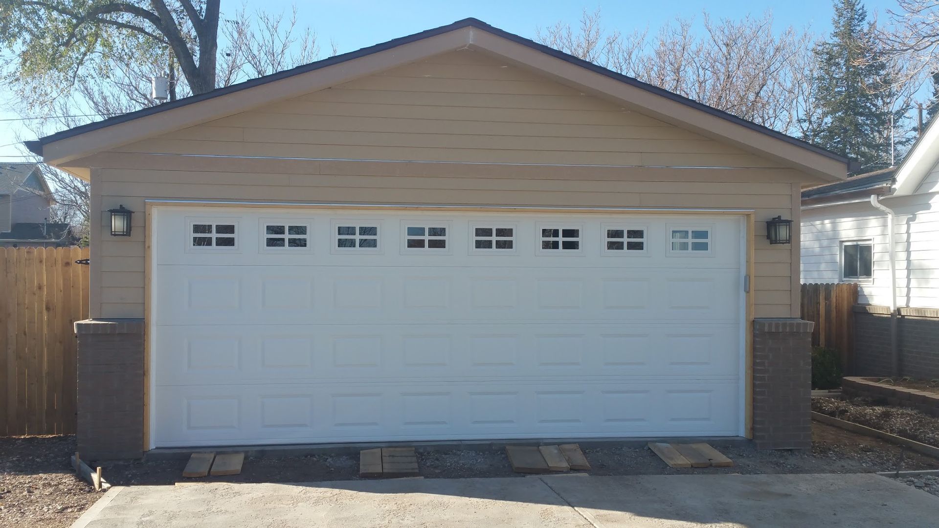 White garage door with square windows, beige siding, and brick pillars.