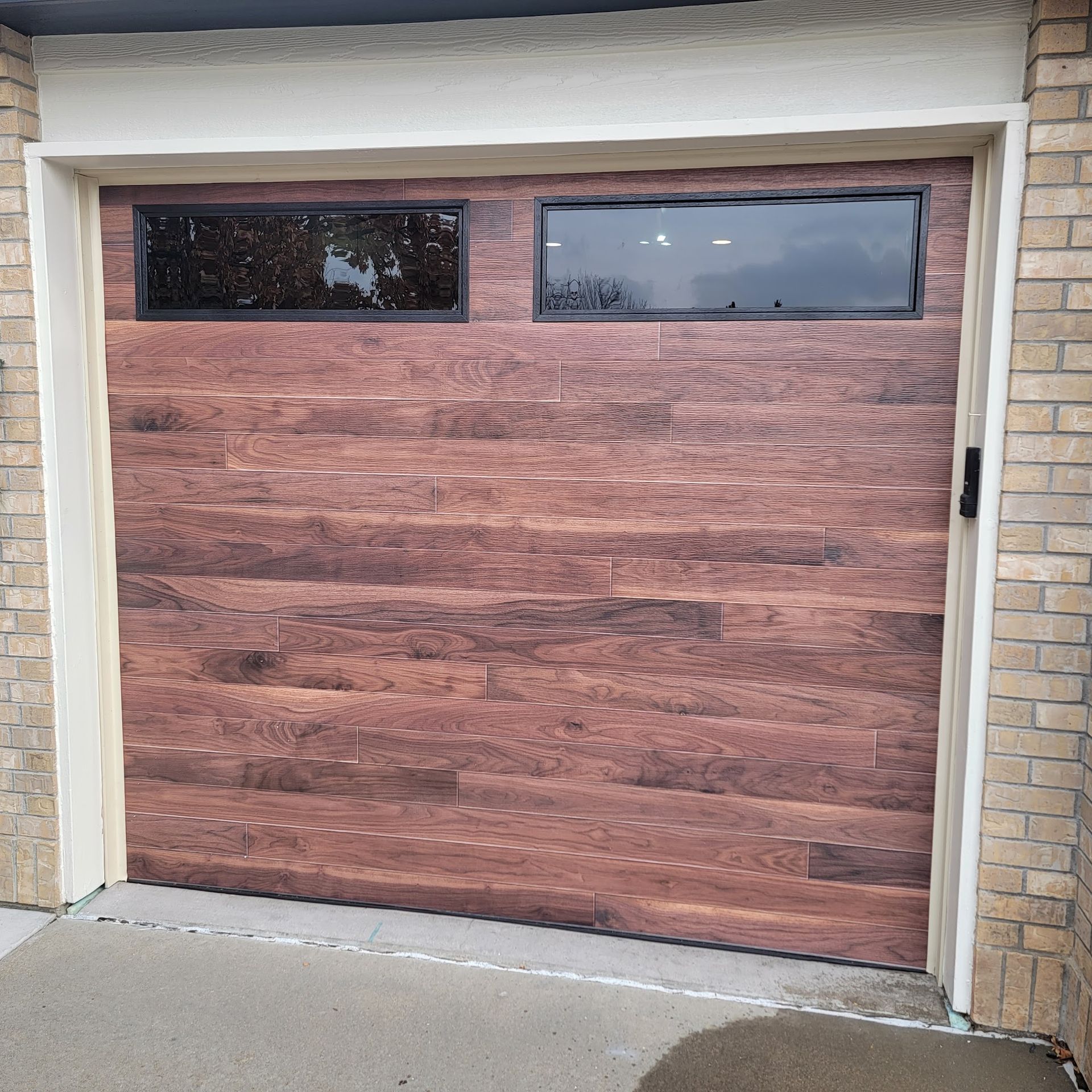 Garage door with wood paneling, two rectangular windows, set in brick building.
