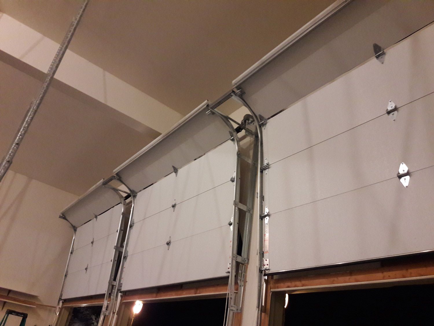 Three white garage doors, partially open, with visible metal tracks and frames.  Inside view of a building.